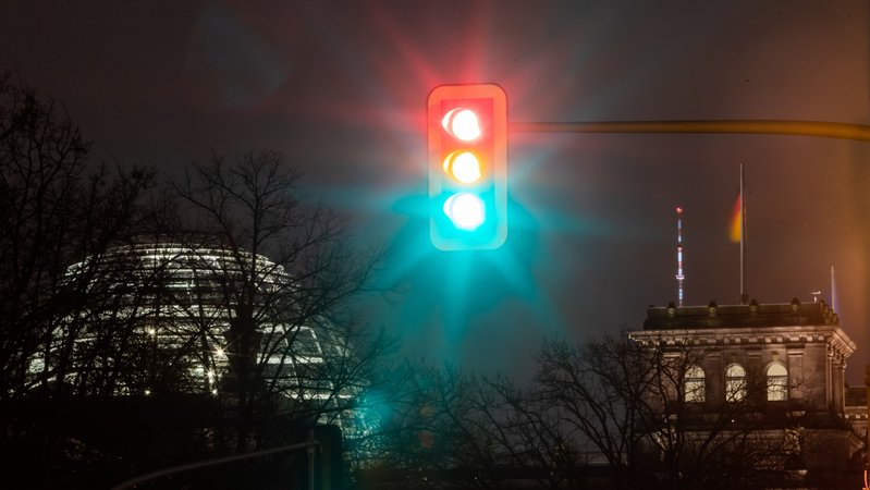 Eine Ampel leuchtet in einer Aufnahme mit Langzeitbelichtung am Morgen vor dem Reichstagsgebäude in allen drei Phasen