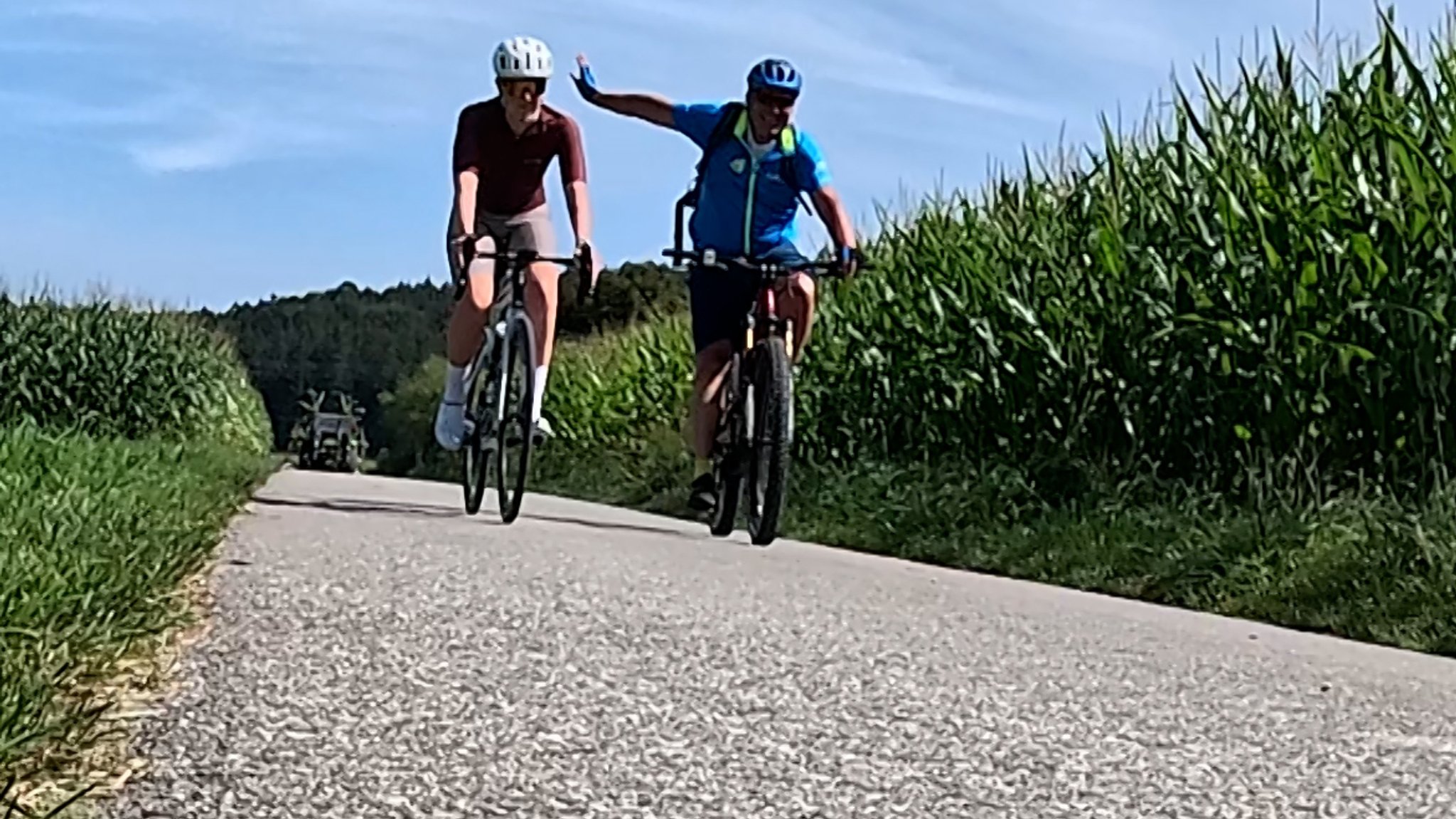 Zwei Radfahrer auf einem geteerten Feldweg.