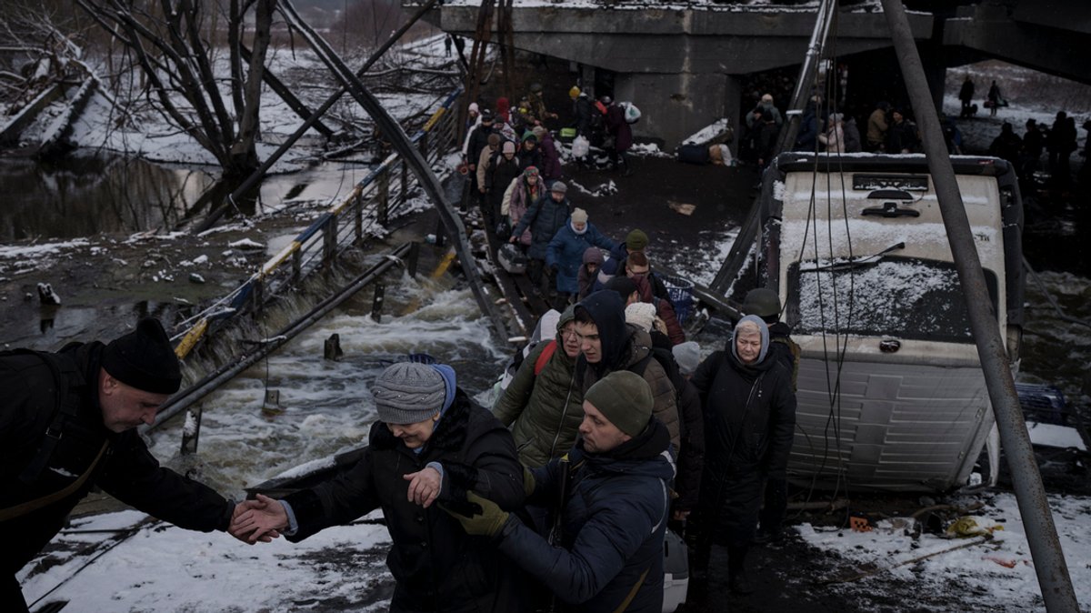 Ukraine: Männer und Frauen überqueren auf der Flucht aus Irpin einen behelfsmäßigen Weg unter einer zerstörten Brücke. Aus der Ukraine sind seit Beginn des russischen Einmarschs mehr als zwei Millionen Menschen geflohen.