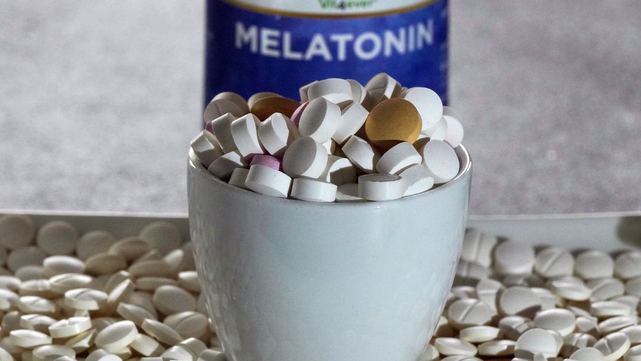 Erhöht Melaton das Risiko für Herzinsuffizienz? Im Bild: Tabletten verschiedener Hersteller liegen in einer Schale vor einer Plastikdose mit der Aufschrift "Melatonin".