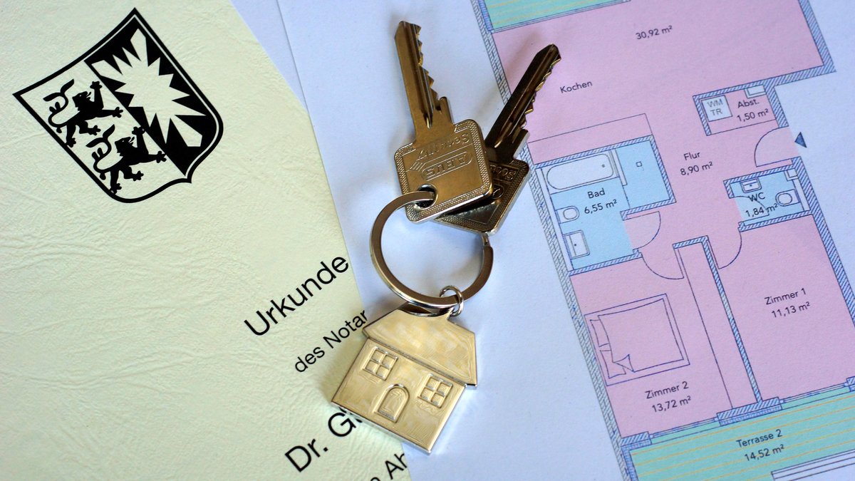 Auf einem ausgedruckten Grundriss und einer notariellen Urkunde liegt ein Schlüssel mit einem Anhänger in Form einen Hauses