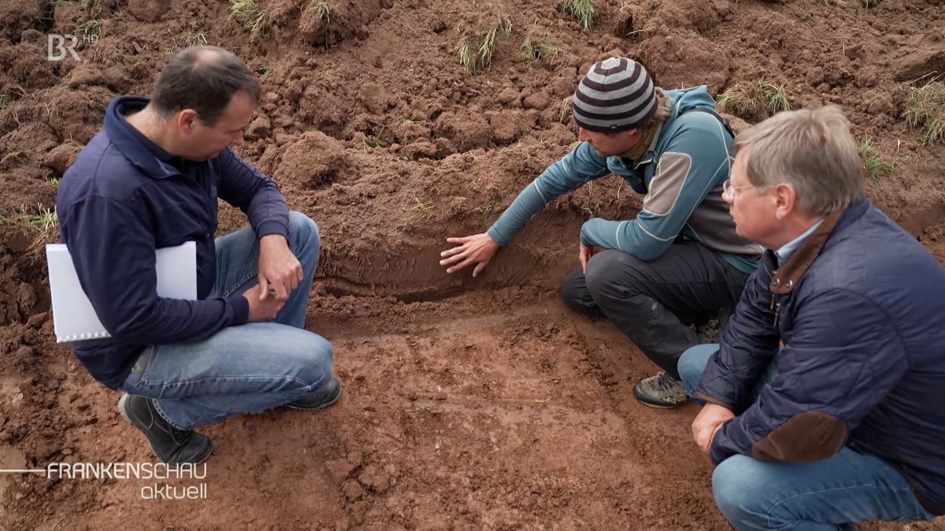 Drei Männer auf dem Acker schauen sich Erde an.