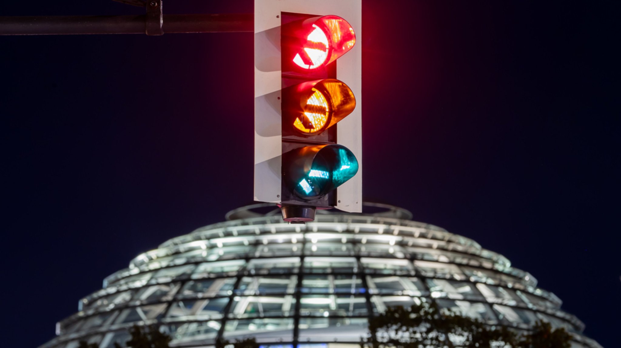 Eine Ampel vor der Kuppel des Reichstagsgebäudes in Berlin leuchtet in einer Langzeitbelichtung in allen drei Phasen. 