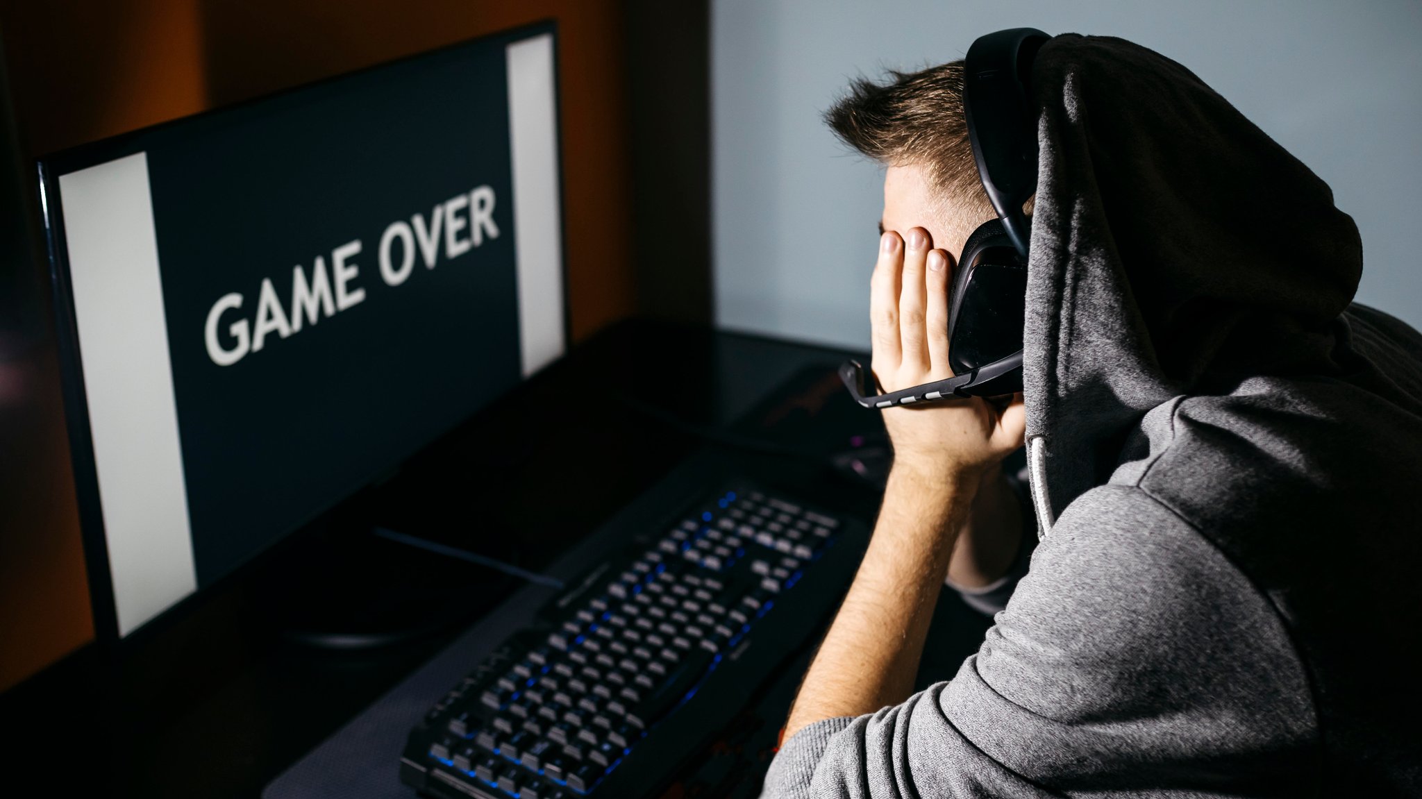 Ein junger Mann vor einem PC-Monitor sitzend, auf dem "Game Over" zu lesen ist.