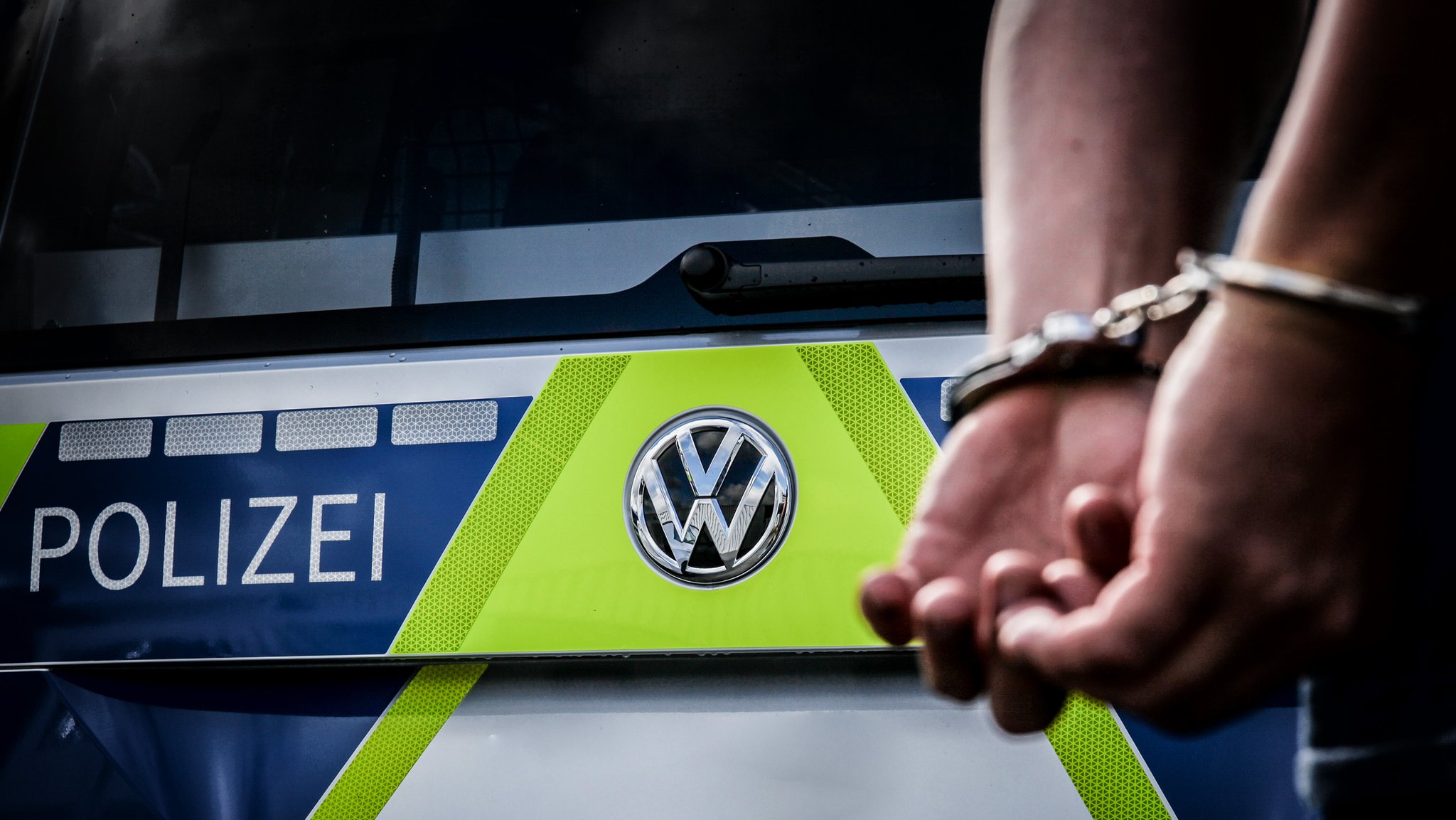 (Symbolbild) Polizeiauto mit Person in Handschließen.