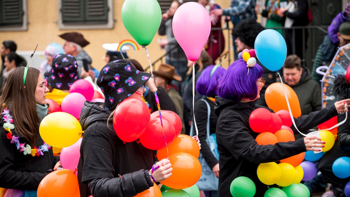 Mit bunten Luftballons behängte Frauen gehen bei einem Faschingszug mit.