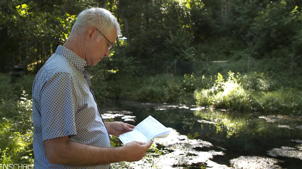 Hydrologe Thomas Ries schaut sich ein Dokument vor einem Bach an.