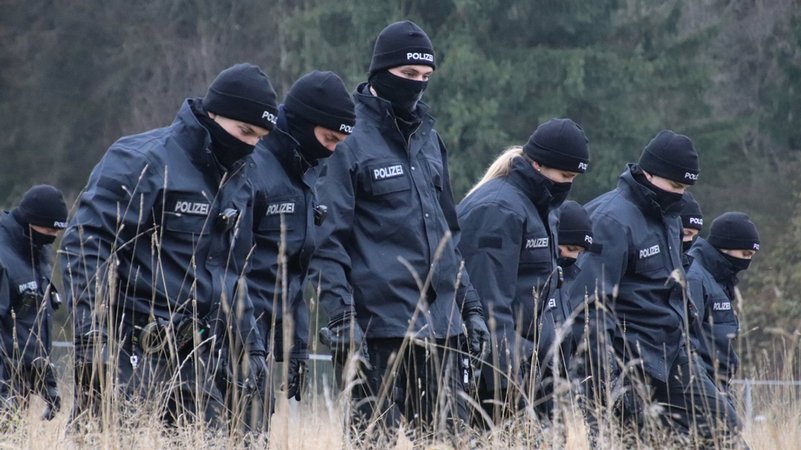 Polizeibeamte mit schwarzer Kleindung und Masken suchen auf einer Wiese Spuren, nachdem in der Nähe des Flughafens Memmingen eine 16-Jährige tot aufgefunden worden ist.