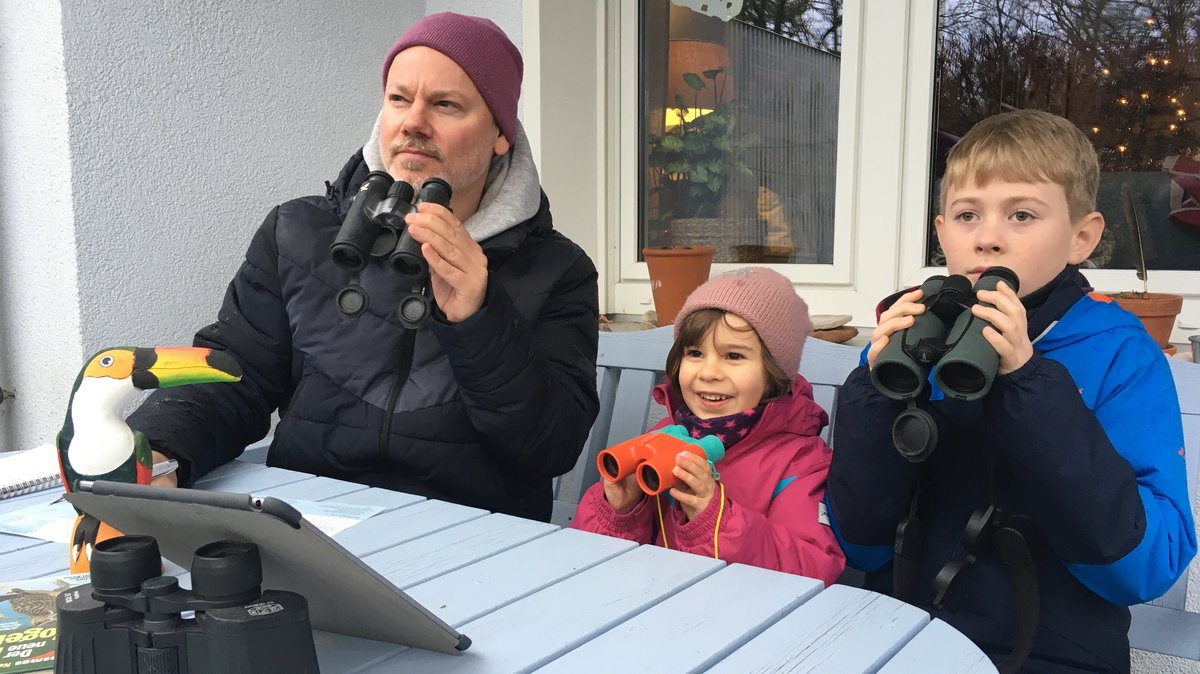 Von links: Tobias Burkert, Philippa und Linus mit Fernglas und Tablet auf der Terrasse.