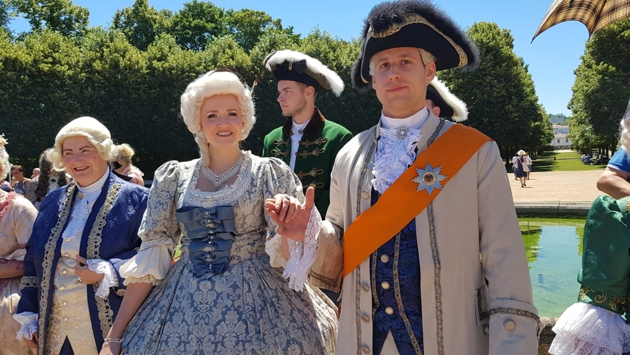 Männer und Frauen in Rokoko-Kostümen und mit Puder-Perücken im Ansbacher Hofgarten.