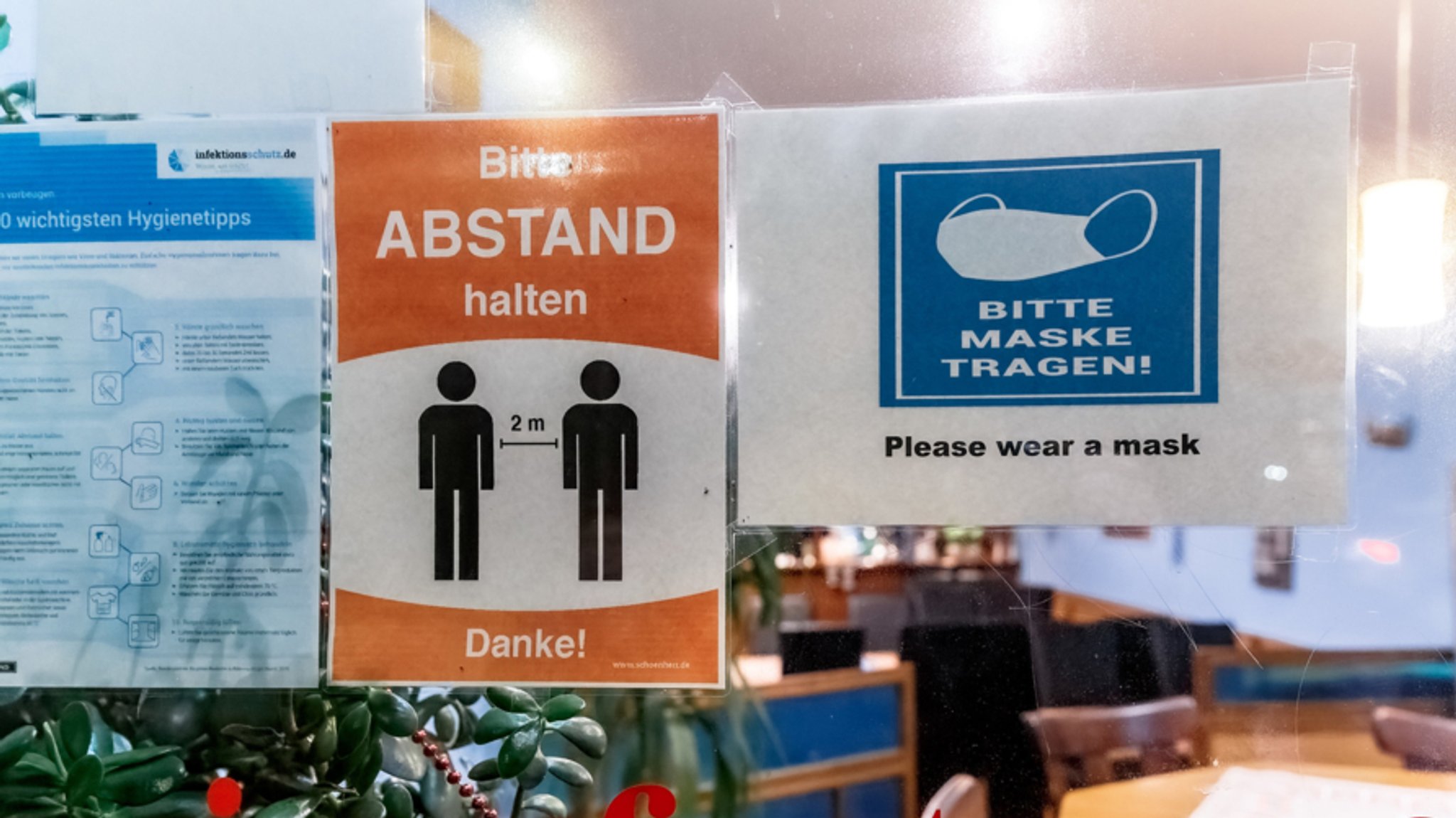 Zettel mit den Aufschriften "Bitte Abstand halten" und "Bitte Maske tragen" hängen an der Tür eines Lokals.  