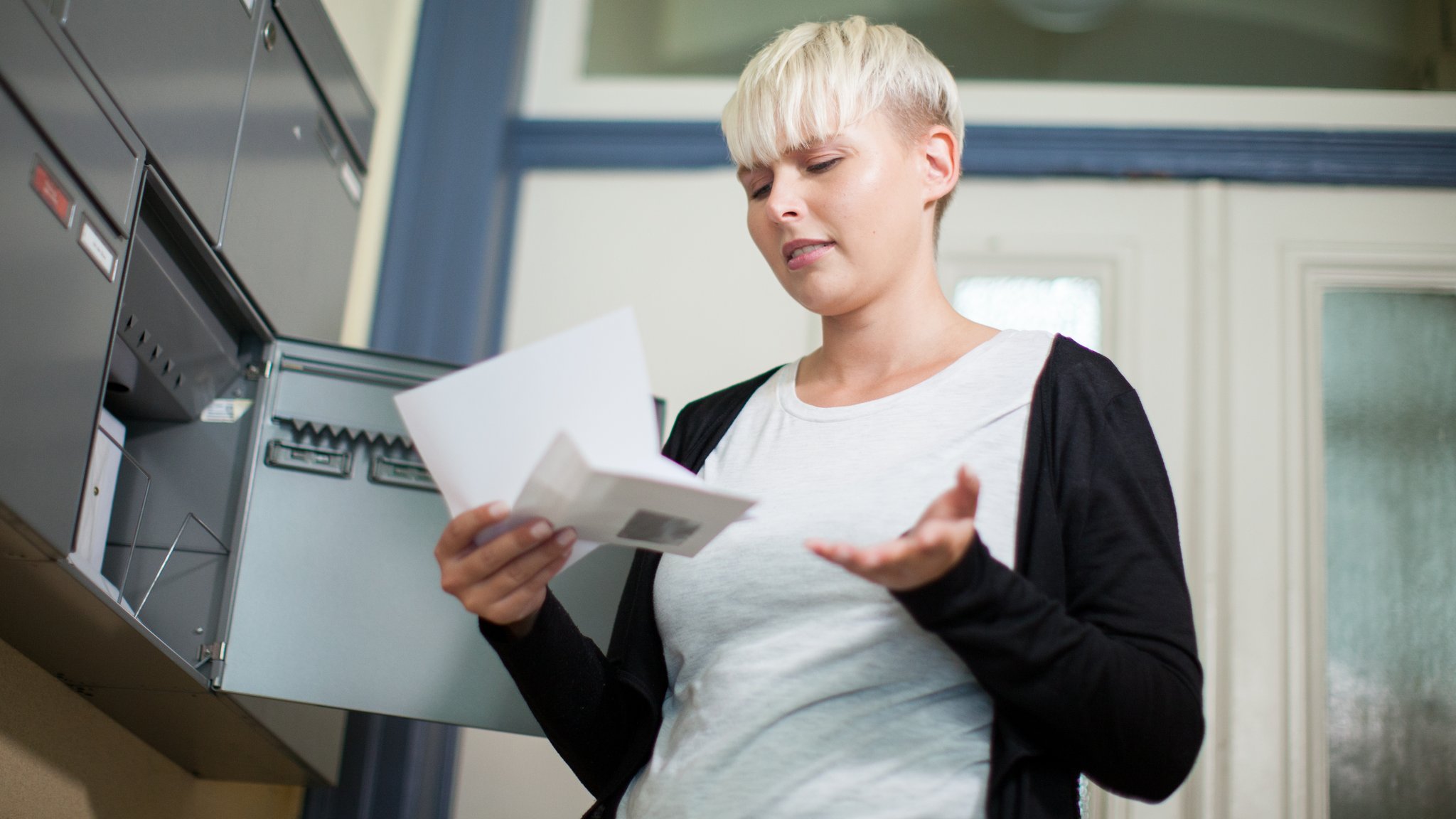 Eine junge Frau steht neben einem Briefkasten und öffnet einen Brief.