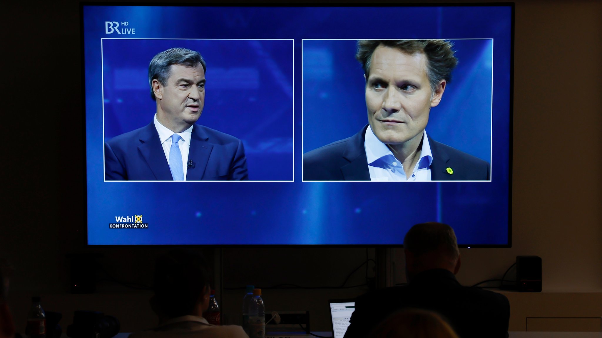 Journalisten schauen im Vorraum zum Fernsehstudio den TV-Schlagabtausch im BR Fernsehen zwischen Markus Söder (l.) und Ludwig Hartmann (r.).