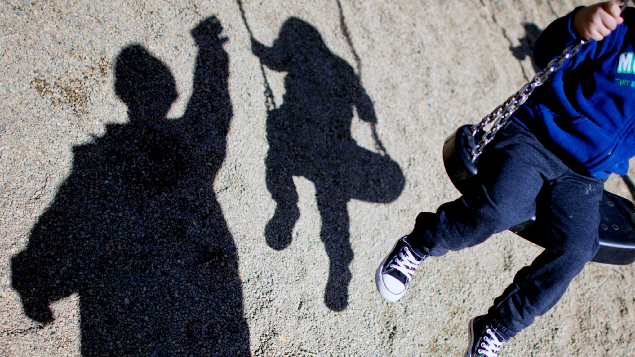 Kind schaukelt, man sieht seinen Schatten und den einer erwachsenen Person