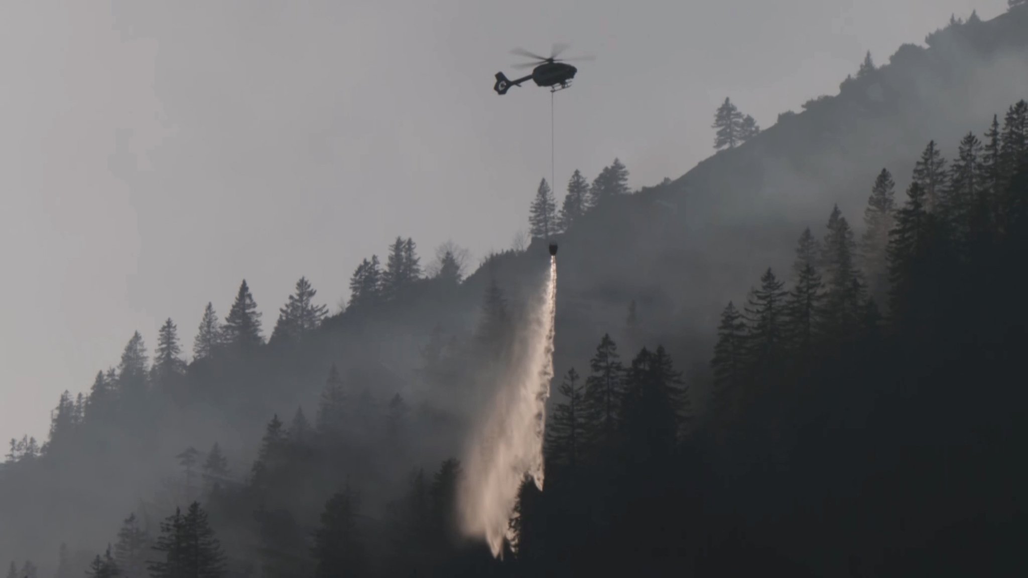 Ein Löschhubschrauber ist im Kampf gegen die Flammen im Bergwald bei Bayrischzell im Einsatz.