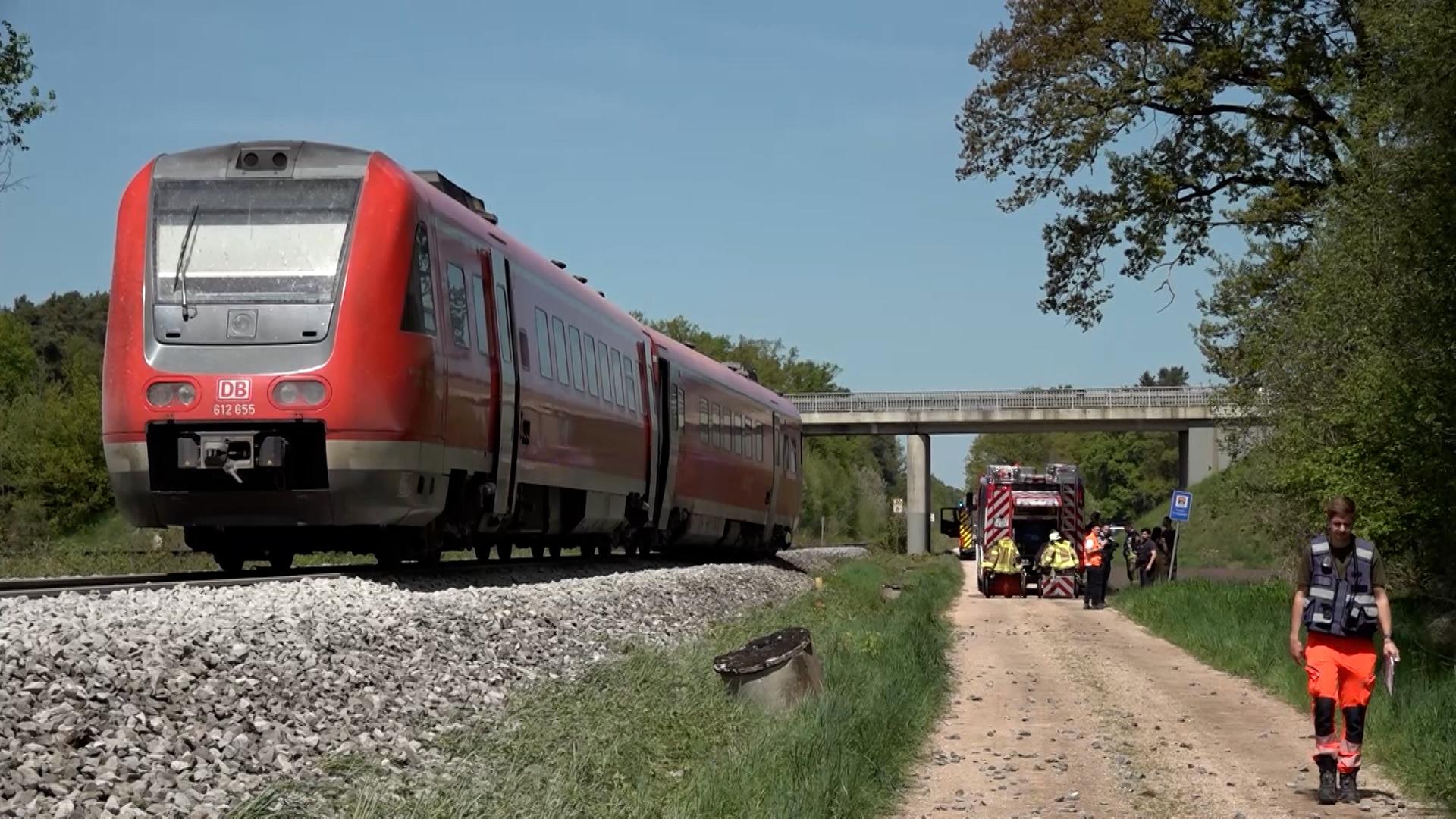 Eine Regionalbahn steht auf einem Gleis im Landkreis Schwandorf. Auf dem parallel verlaufenden Feldweg steht ein Feuerwehrauto, mehrere Rettungskräfte sind zu Fuß unterwegs. 