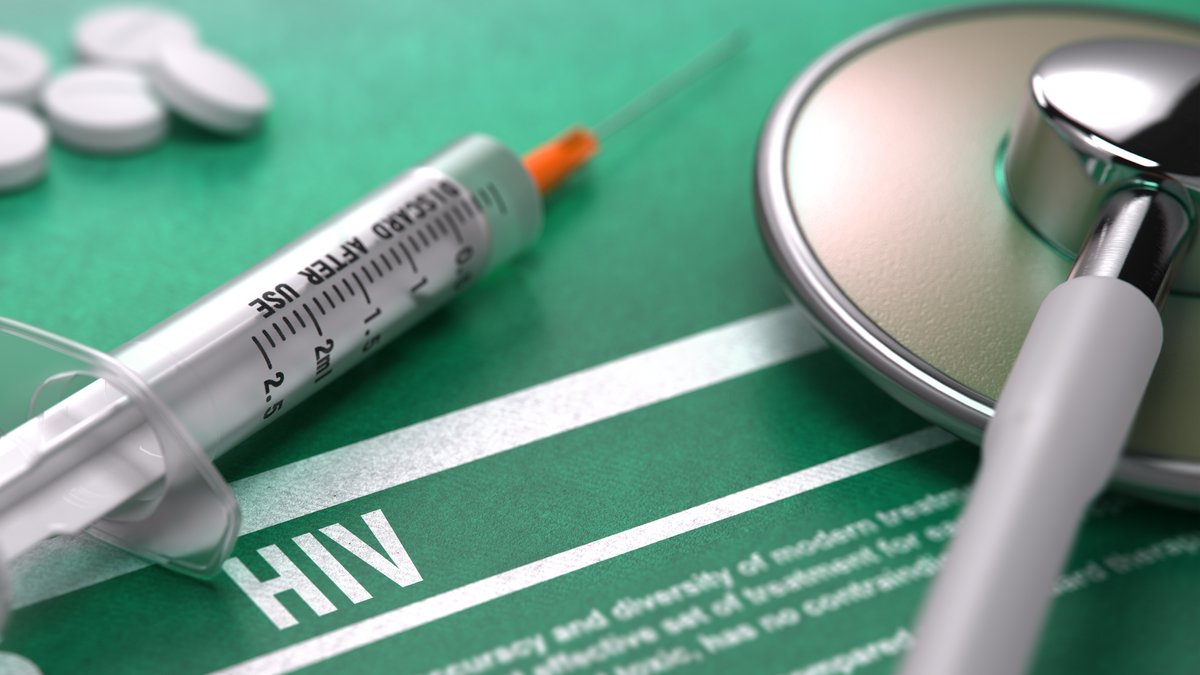 Tabletten, Spritze und Stethoskop auf grünem Hintergrund mit dem Schriftzug HIV.