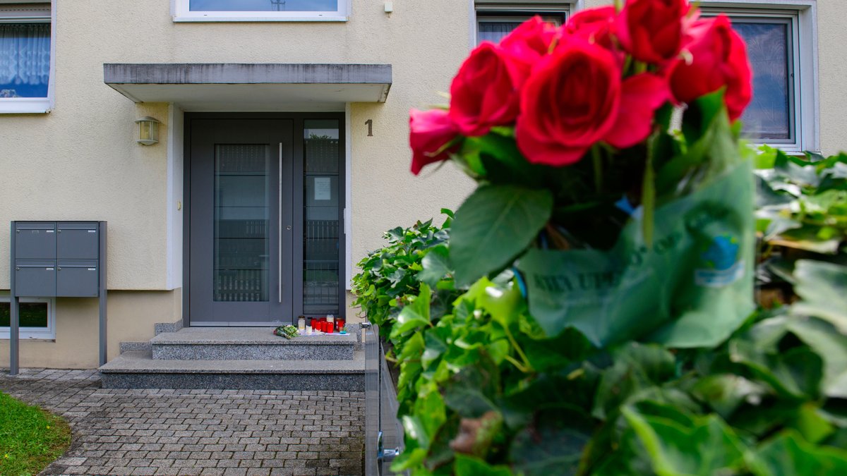 Blumen und Kerzen liegen auf einem Hauseingang. In diesem Haus wurden drei Bewohner erschossen. 