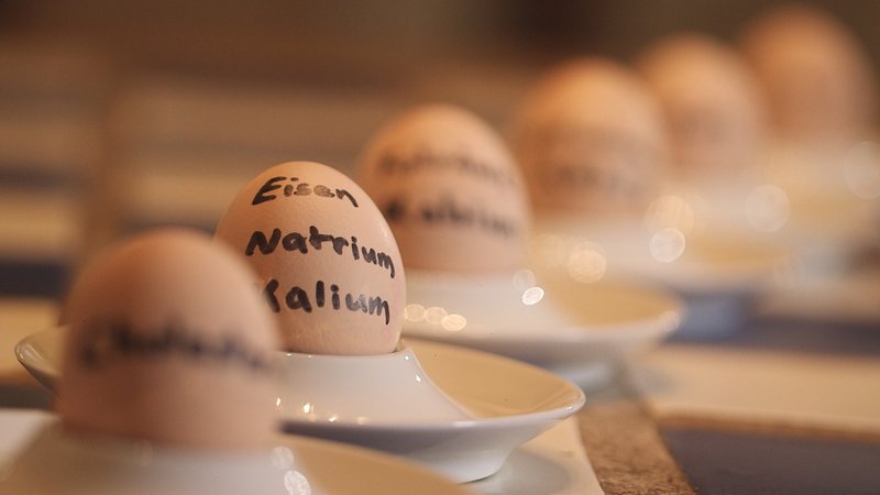 Hühnereier in Eierbecherern mit Schriftzug Eisen, Natrium, Kalium etc.