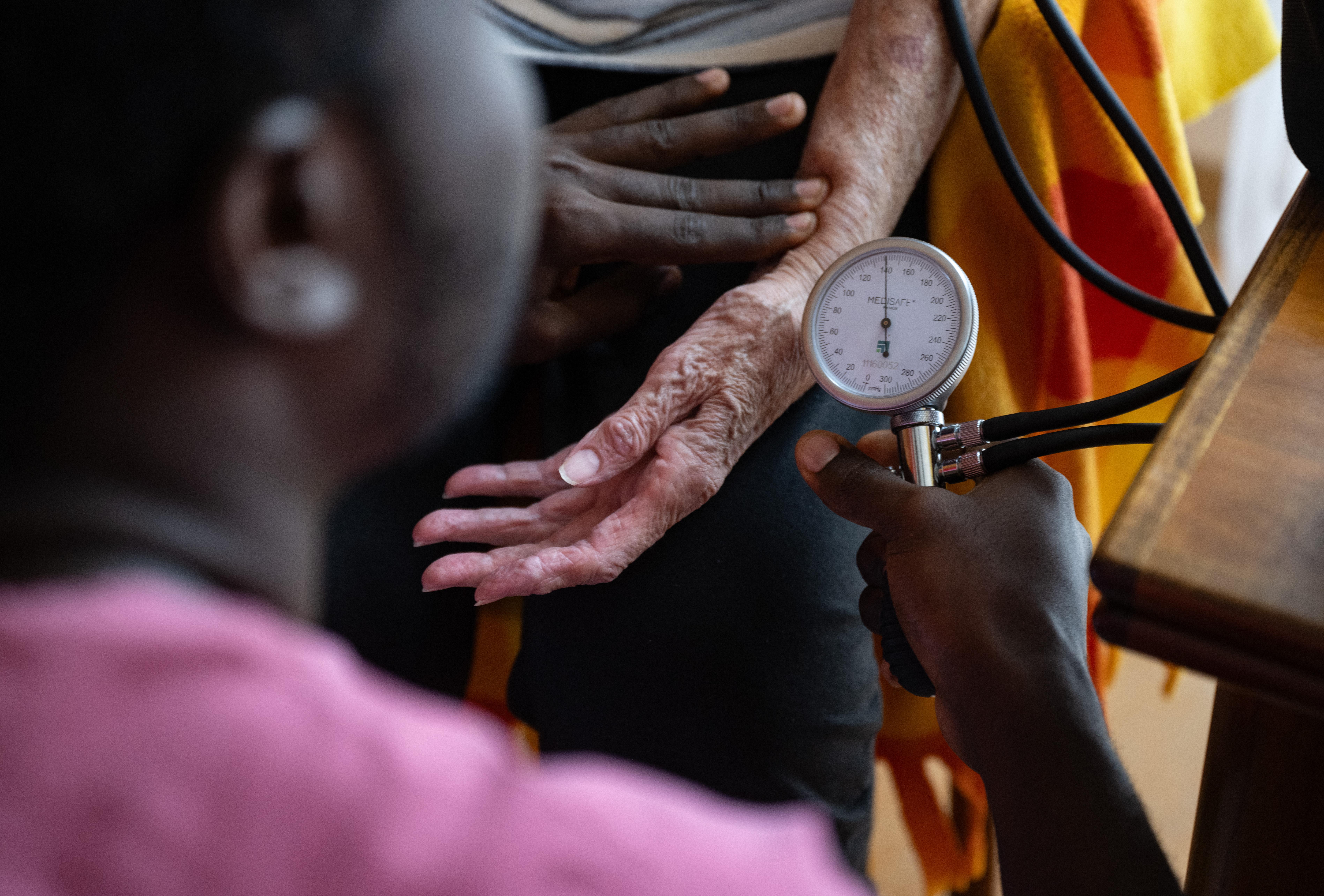 Ein Auszubildender zum Pflegefachmann misst den Blutdruck einer Seniorin.