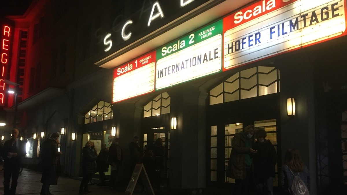 Menschen stehen vor dem Kino "Scala" in Hof. Auf beleuchteten Tafeln steht "Internationale Hofer Filmtage".