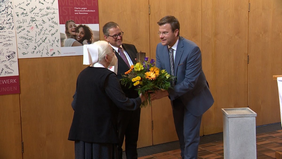 Nürnbergs Oberbürgermeister Markus König übergibt einer Diakonisse und einem Mann im Anzug einen Blumenstrauß.