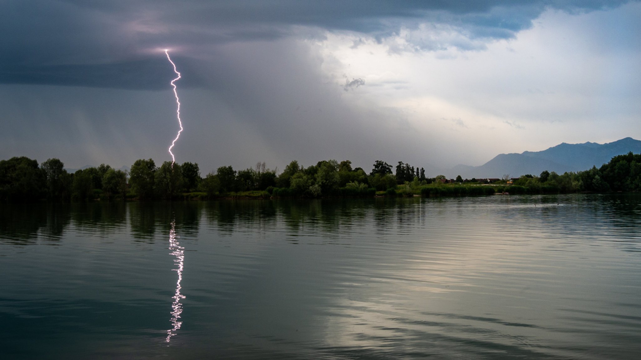 Eine Gewitterfrontzieht mit einem einschlagendem Blitz über einem Alpensee in Bayern auf. | Bild: stock.adobe.com/Vincent Eine Gewitterfrontzieht mit einem einschlagendem Blitz über einem Alpensee in Bayern auf.