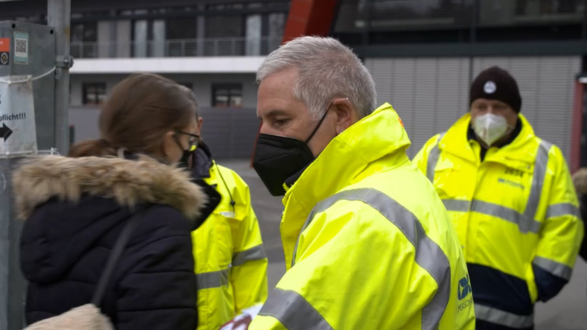 Drei Sicherheitsleute in gelben Warnjacken kontrollieren am Eingang zum Sportpark Valznerweiher