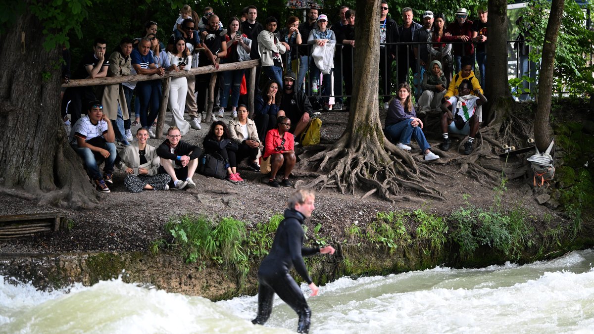 Blick auf den Münchner Eisbach und Zuschauer am Ufer.