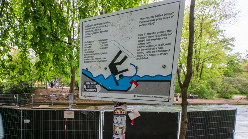 Der Eisbach in München ist bis auf weiteres abgesperrt. Warnschilder weisen auf die Gefahren der künstlichen Welle hin. | Bild: Peter Kneffel/dpa Der Eisbach in München ist bis auf weiteres abgesperrt. Warnschilder weisen auf die Gefahren der künstlichen Welle hin.