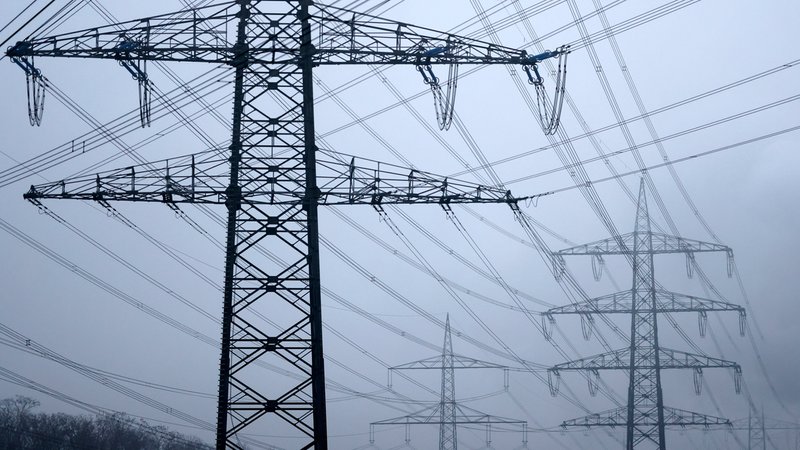 Strommasten stehen auf einem Feld in der Nähe von Industrieanlagen bei Köln. | Bild: picture alliance / Panama Pictures | Christoph Hardt Strommasten stehen auf einem Feld in der Nähe von Industrieanlagen bei Köln.