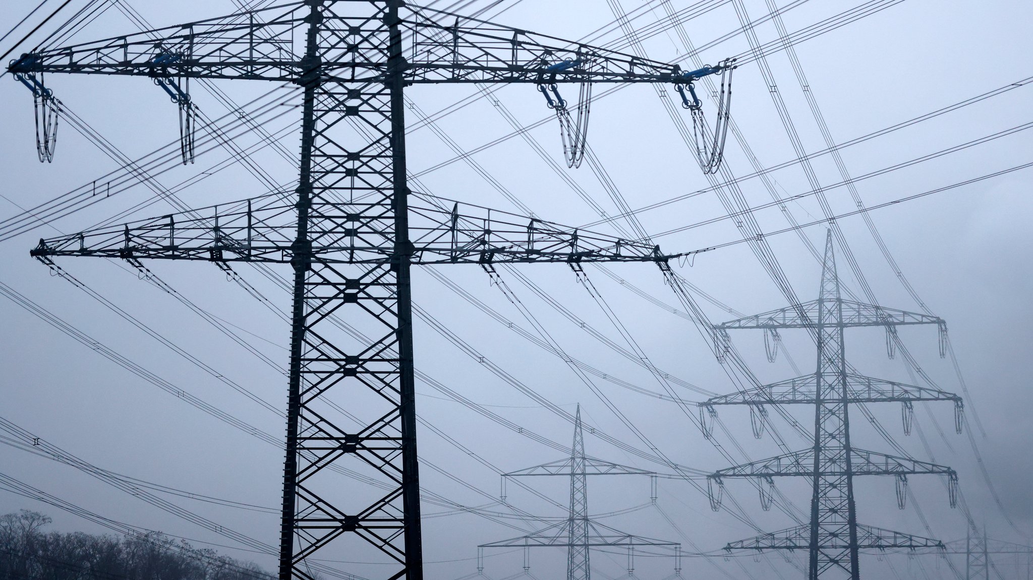 Strommasten stehen auf einem Feld in der Nähe von Industrieanlagen bei Köln. 