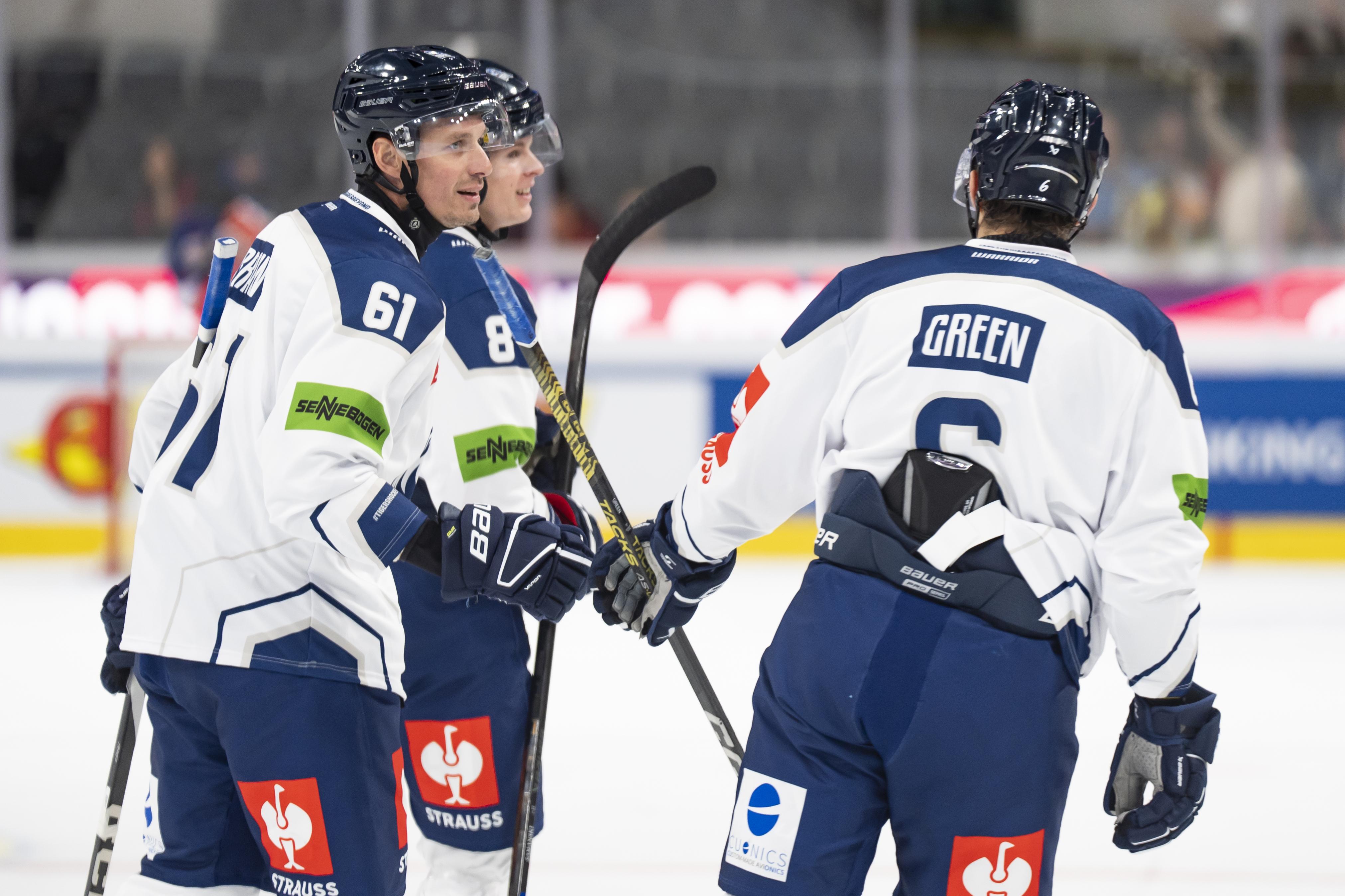 Drei Eishockeyspieler der Straubing Tigers stehen während eines Spiels gemeinsam auf dem Eis und halten ihre Schläger.