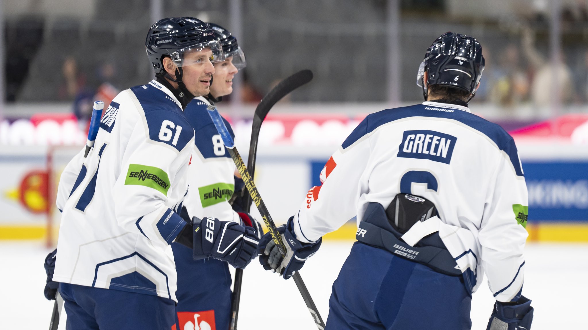 Drei Eishockeyspieler der Straubing Tigers stehen während eines Spiels gemeinsam auf dem Eis und halten ihre Schläger.