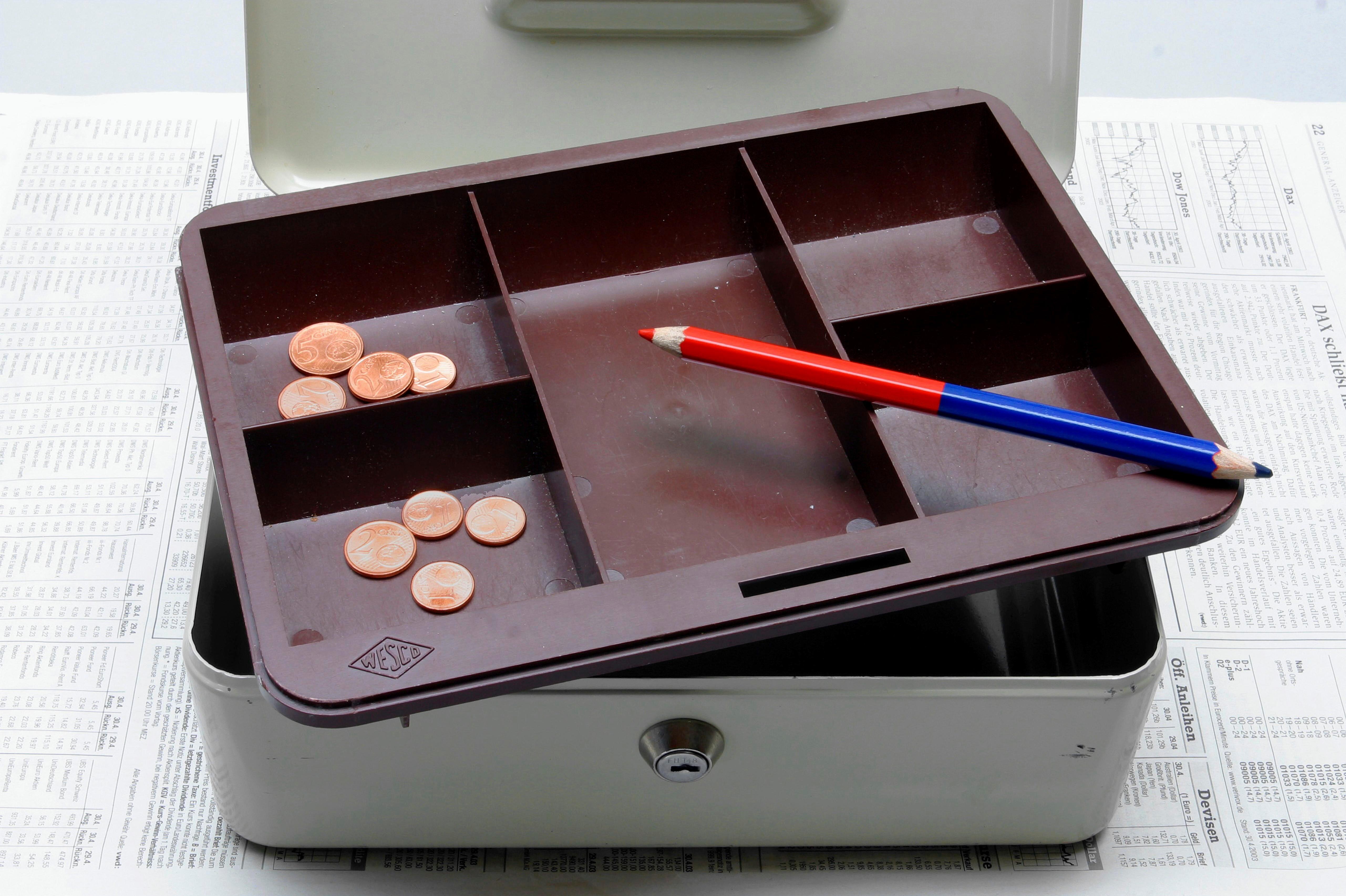 Eine leere Kasse, in der nur noch ein paar Cent-Münzen liegen. Auch ein Rotstift liegt darin. 