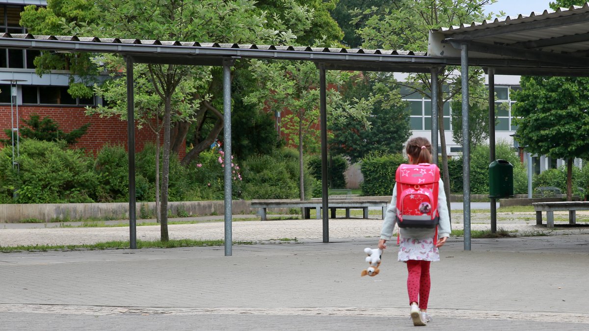 Ein Mädchen geht alleine über einen Schulhof.