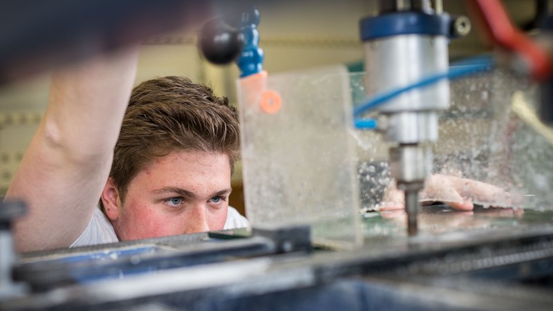 Ein Auszubildender zum Glaser bohrt am 04.05.2015 in der Werkstatt einer Glaserei in Taunusstein (Hessen) mit einem Diamantbohrer ein Loch in eine Glasscheibe. | Bild: picture alliance / dpa Themendienst | Frank Rumpenhorst Ein Auszubildender zum Glaser bohrt am 04.05.2015 in der Werkstatt einer Glaserei in Taunusstein (Hessen) mit einem Diamantbohrer ein Loch in eine Glasscheibe.