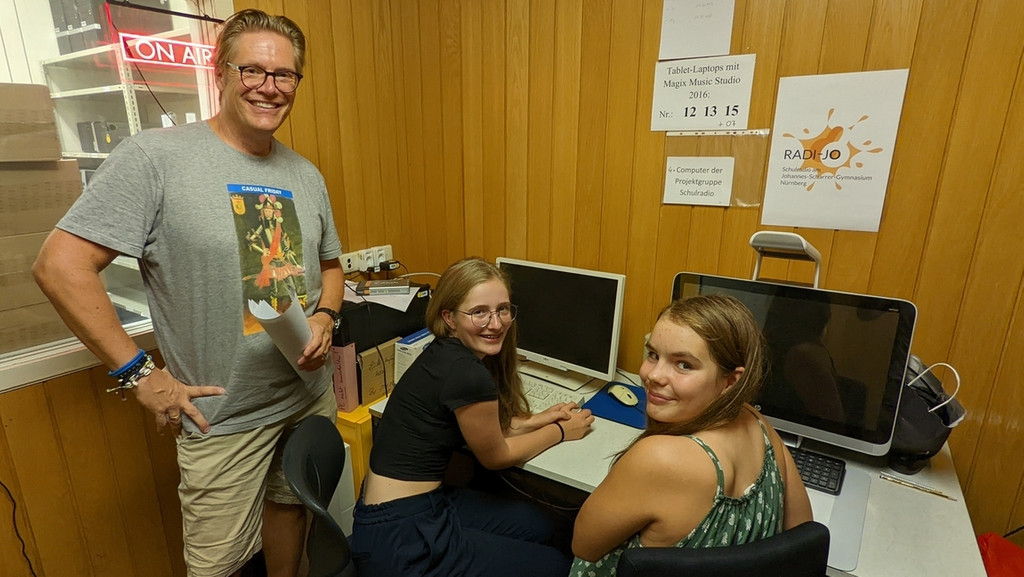 Ein Mann und zwei jugendliche Mädchen sitzen vor zwei Computern.