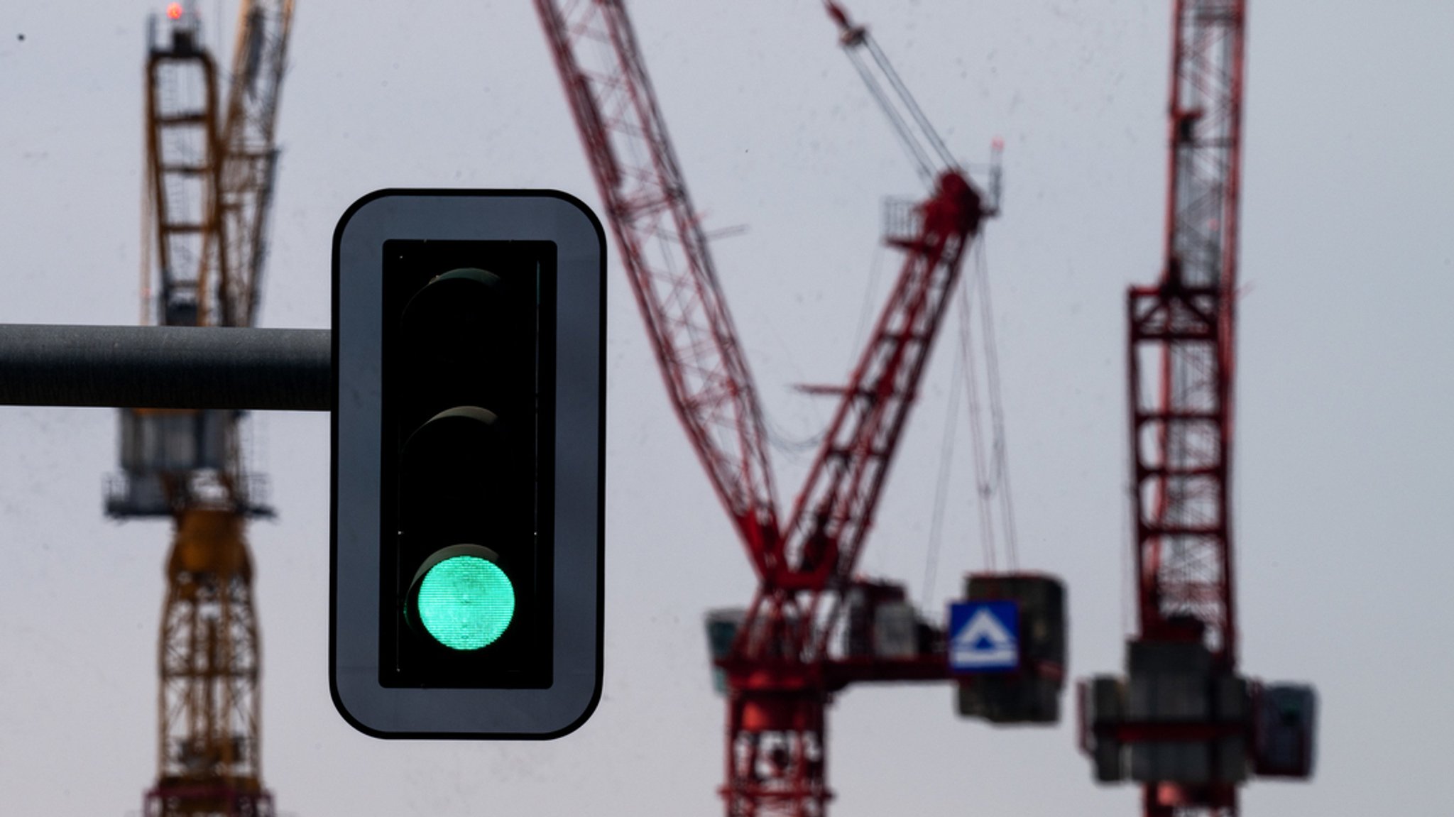 Eine Grün zeigende Ampel vor der Kulisse von Kränen auf einer Baustelle. 