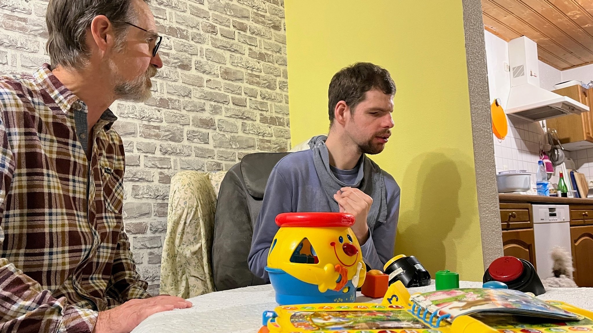 Stefan (r.) sitzt im Wohnzimmer und spielt. Sein Vater weicht nicht von seiner Seite.