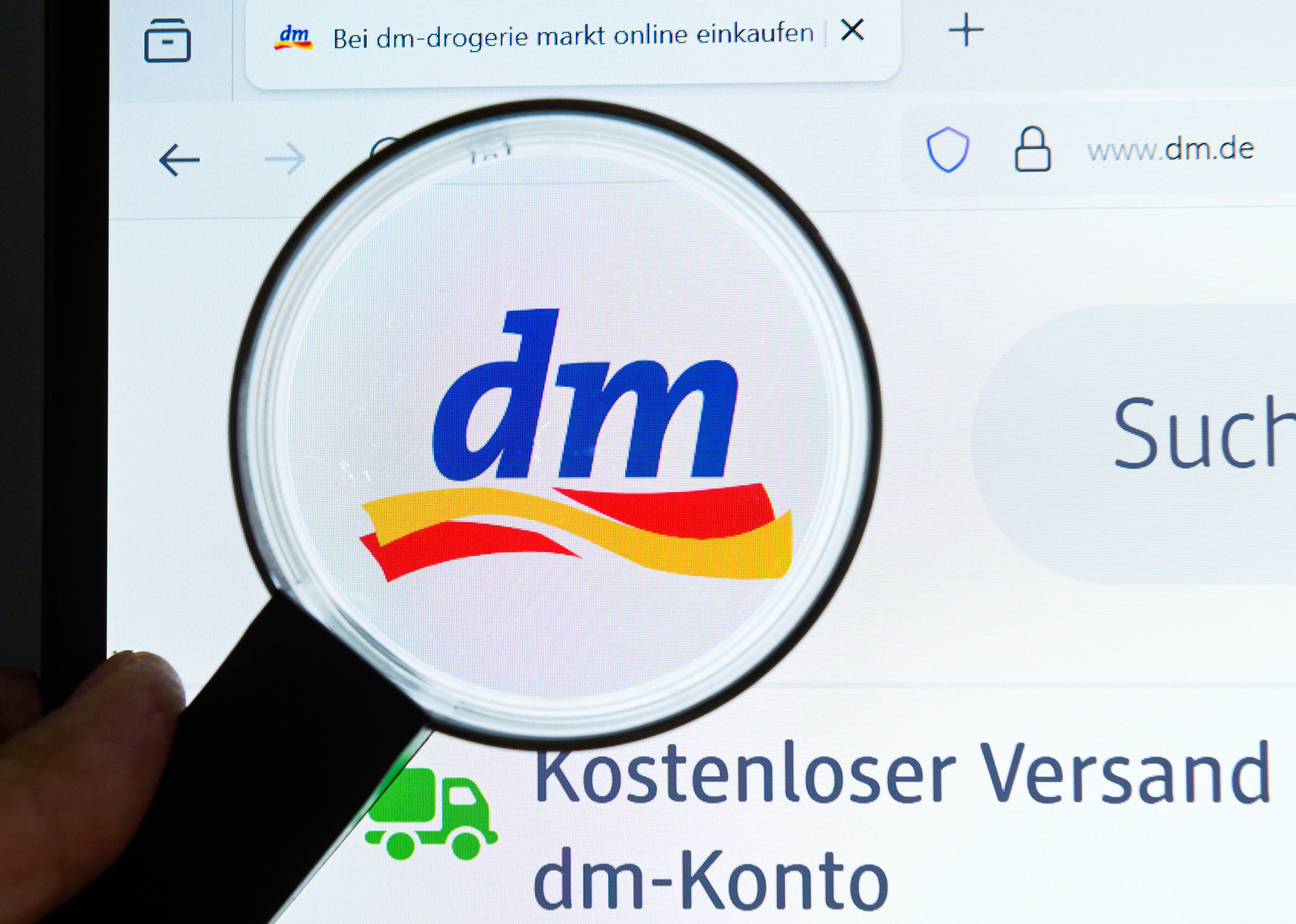 Auf dem Bild ist eine Lupe zu sehen, die das dm-Logo auf einem Bildschirm untersucht