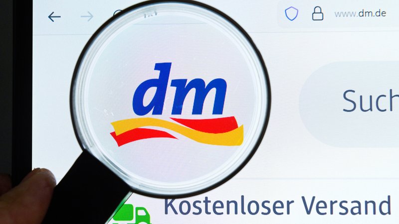 Auf dem Bild ist eine Lupe zu sehen, die das dm-Logo auf einem Bildschirm untersucht | Bild: picture alliance / Joko | Joko Auf dem Bild ist eine Lupe zu sehen, die das dm-Logo auf einem Bildschirm untersucht