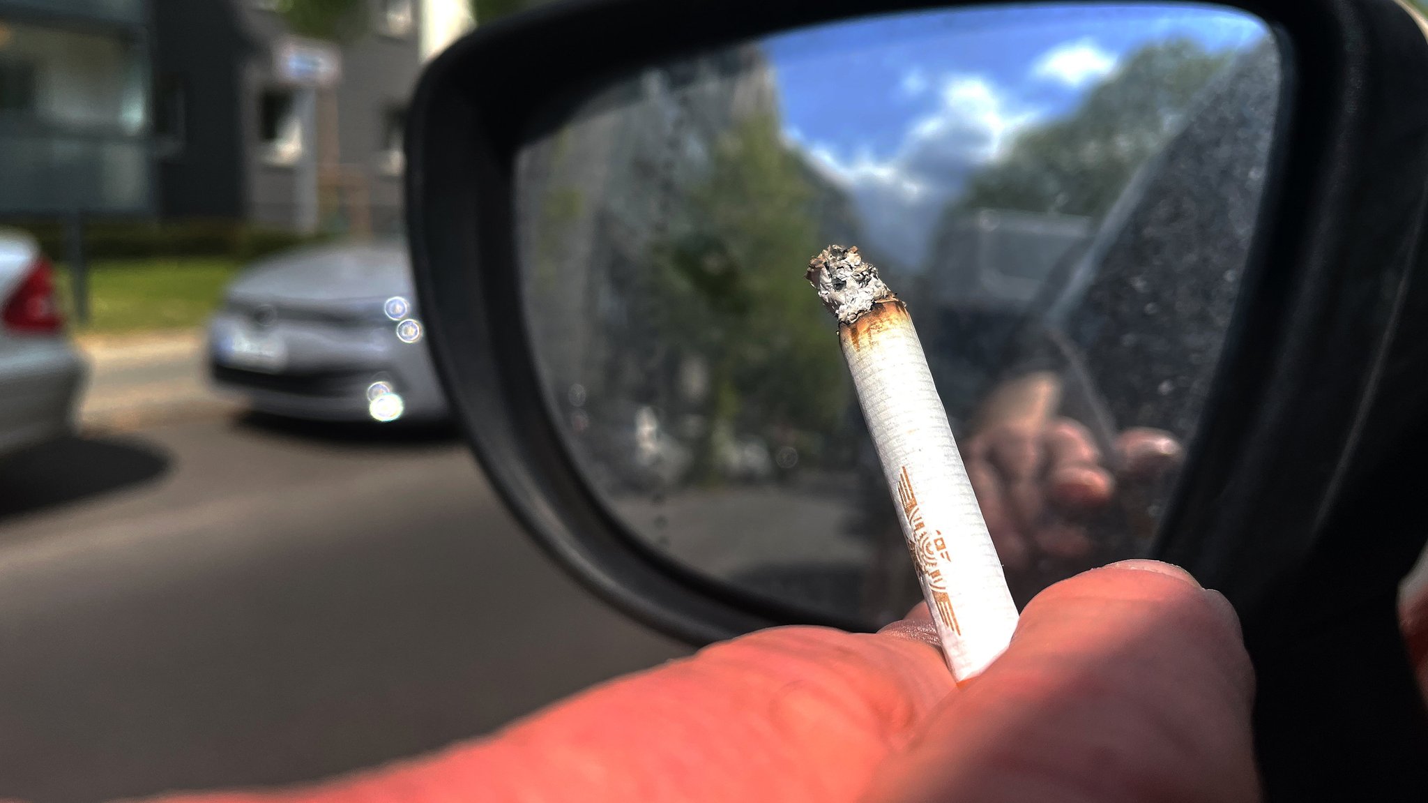 Eine Person raucht eine Zigaretten beim Autofahren.