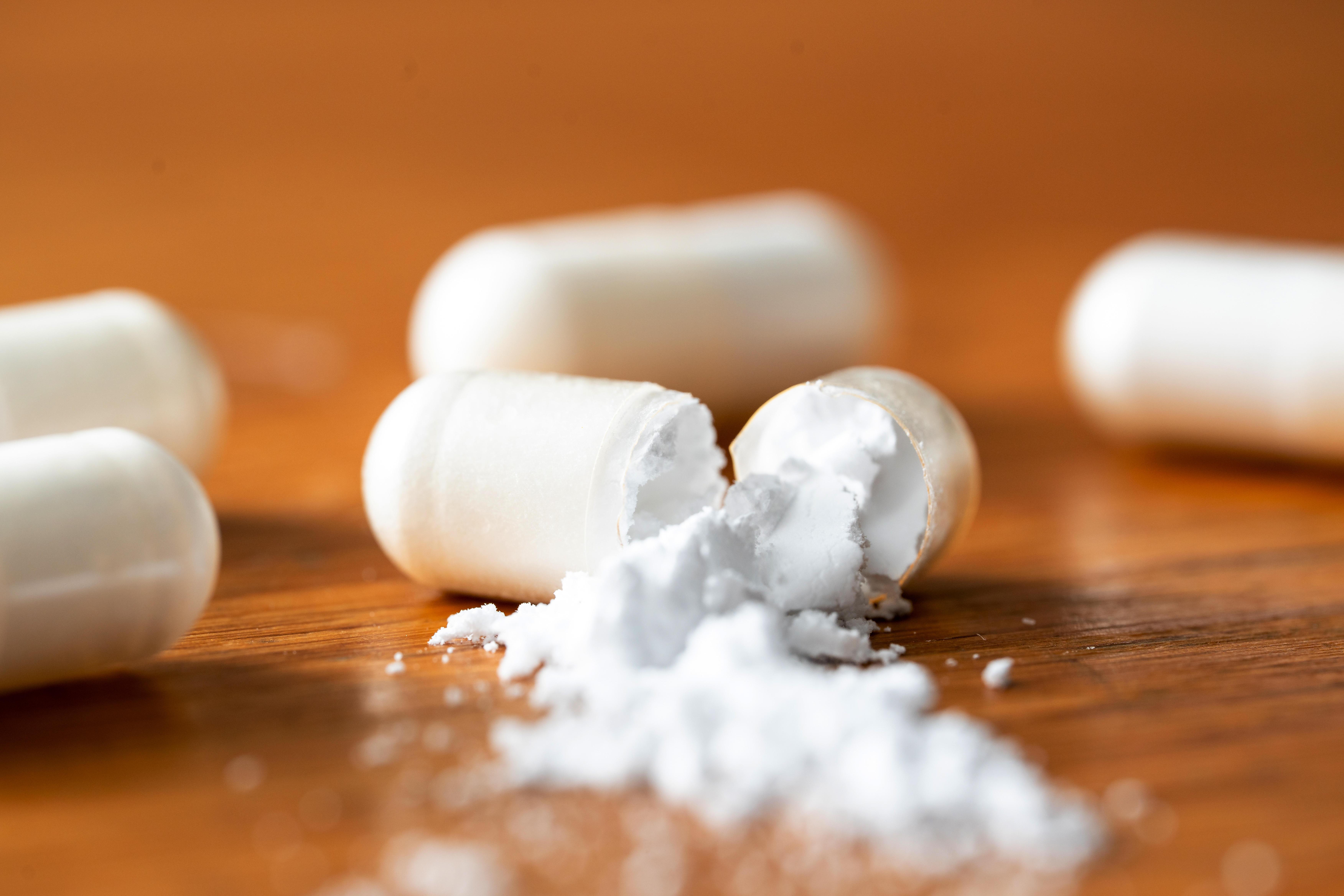 Geteilte, weiße Tabletten aus denen Pulver rieselt. Symbolbild für Kreatin
