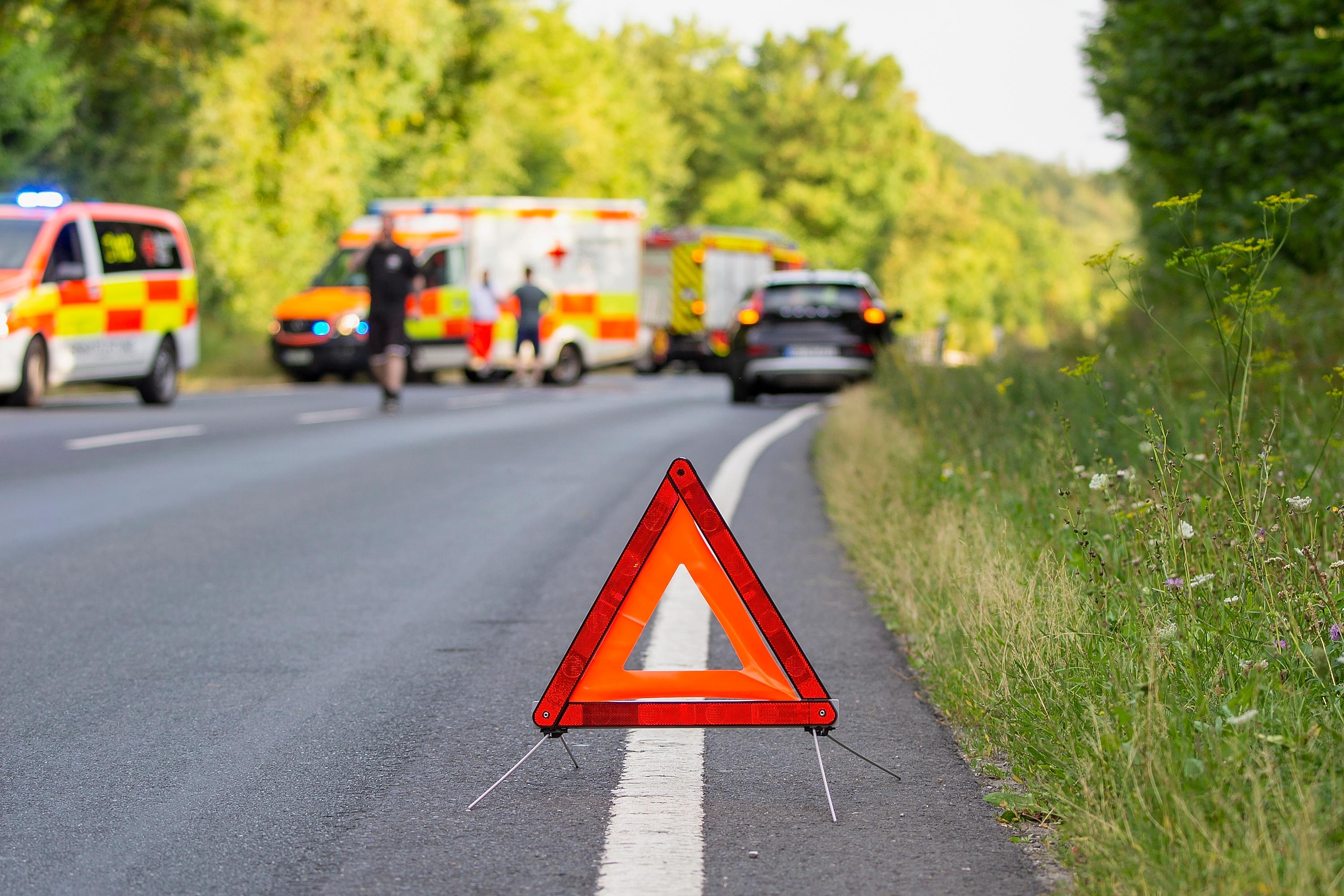 Auf dem Bild ist ein Warndreieck auf einer Landstraße zu sehen. Im Hintergrund sind mehrere Eisnatzfahrzeuge