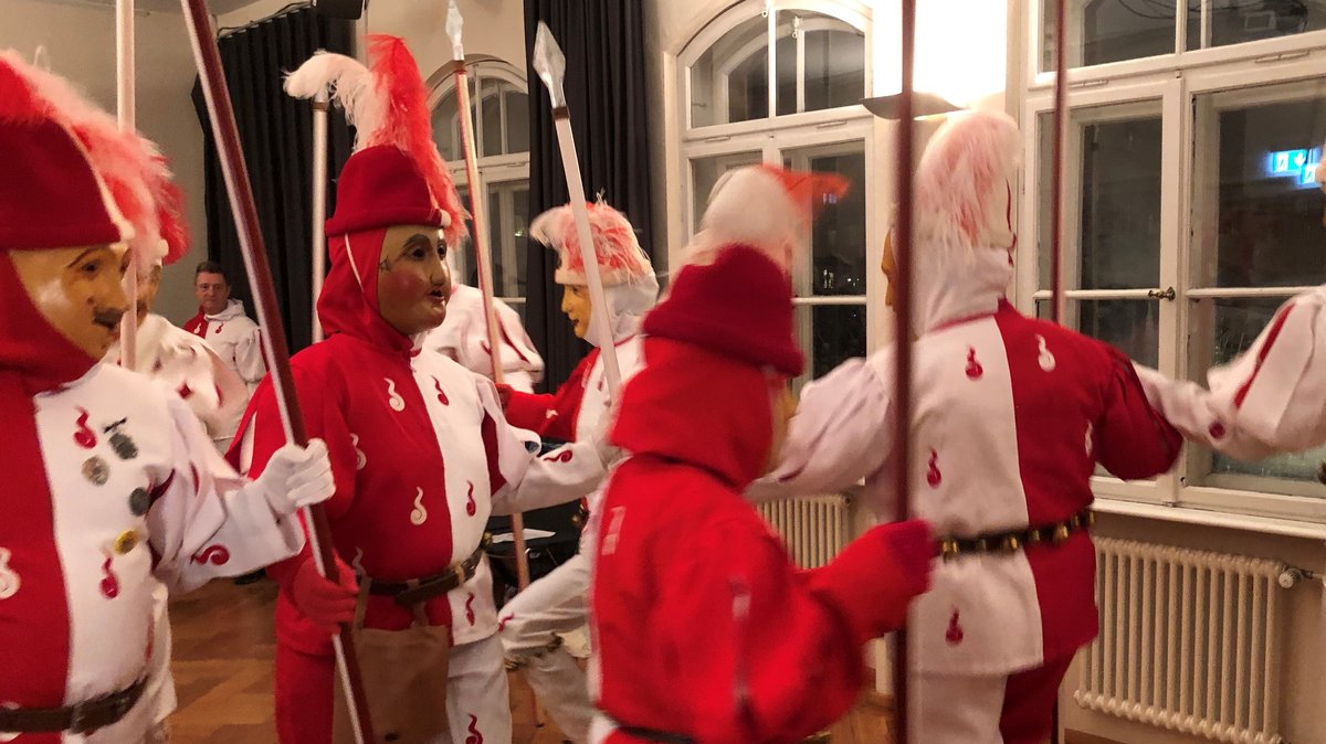 Rot-weiße Gestalten mit Holz-Gesichtsmasken tanzen im Kreis.