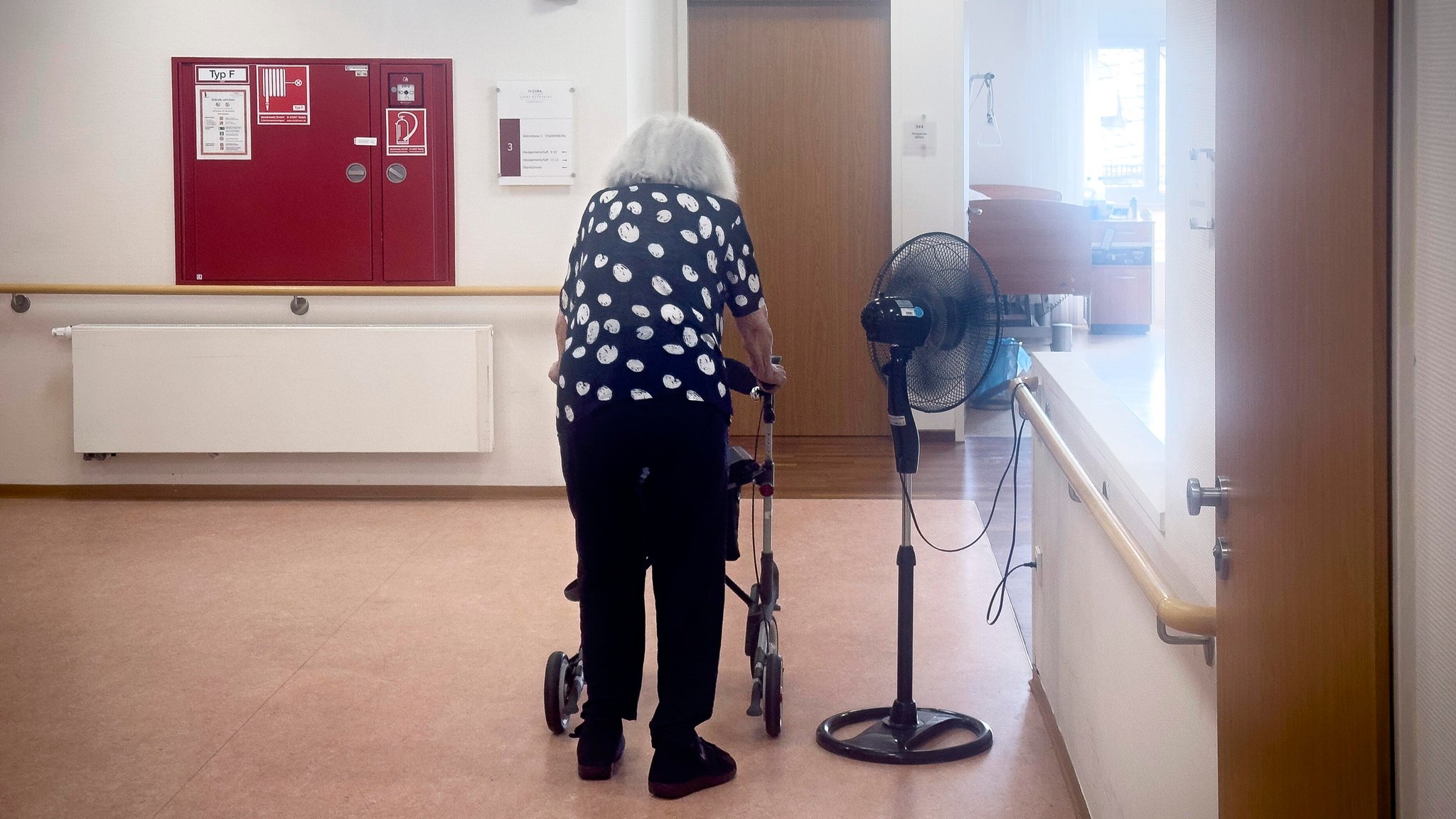 Alte und behinderte Frau mit Rollator in einem Flur von einem Altersheim.