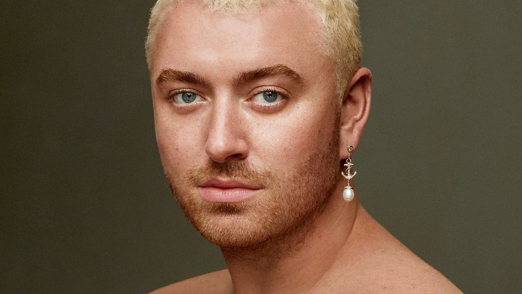 Ein Portraitbild des Musikers Sam Smith mit nacktem Oberkörper, blondierten Haaren und einem Ohrring mit Anker und Perle: