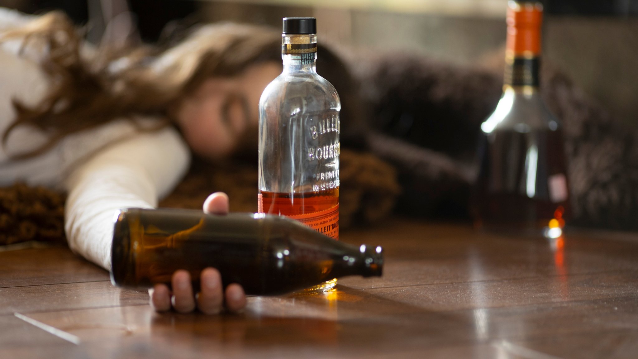 Eine Frau liegt auf dem Boden und hält eine leere Flasche Bier in der Hand