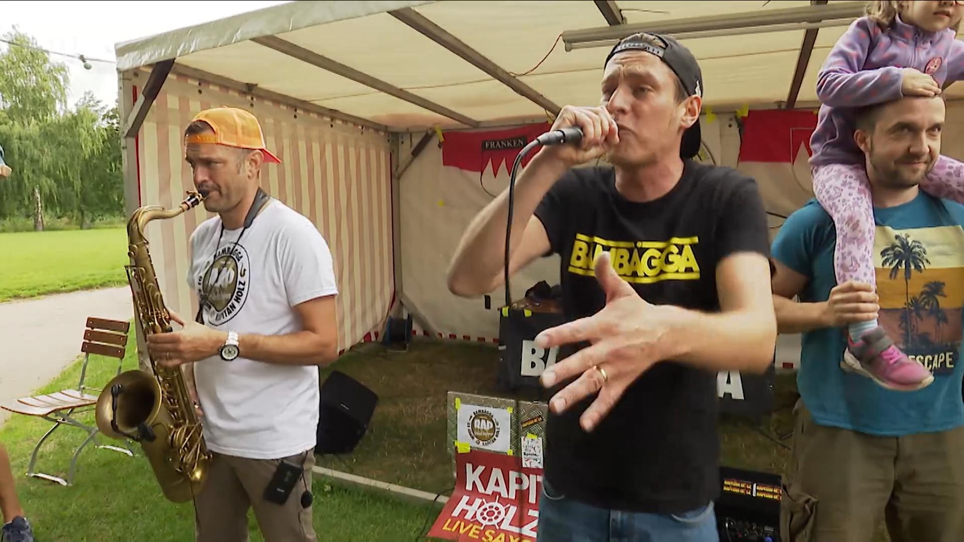 Ein Musiker mit Saxophon und ein Sänger am Mikrophon geben ein Konzert.  | Bild:BR